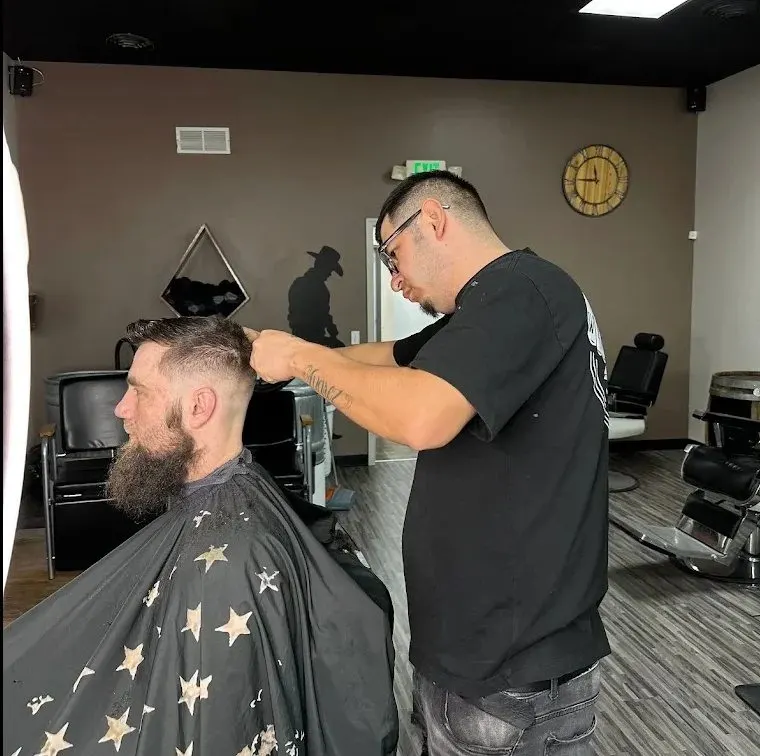A barber at work under the cowboy wall art inside Saloon Cuts